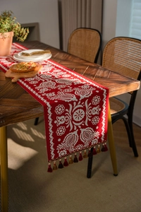 Macro detail of red woven table runner with white floral motifs and fringe tassels
