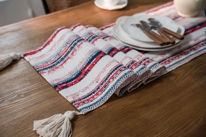 Detail of bohemian geometric table runner with red and blue patterns and cotton tassels