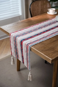 Detail of bohemian table runner with red blue geometric patterns and cream tassels