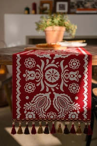 Close-up of red jacquard table runner with white floral patterns and colorful tassels