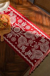 Detail of red table runner with white ethnic floral pattern on a wooden table surface