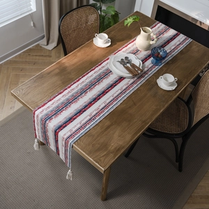 Ethnic style table runner with red blue geometric patterns and cream tassels on wood