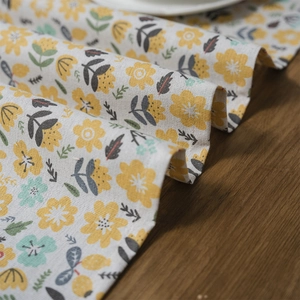 Floral print table runner with yellow flowers and tassels on a wooden surface
