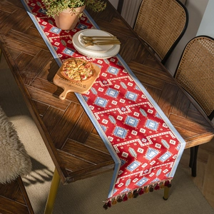Red jacquard table runner with geometric boho patterns and elegant tassels on wood table