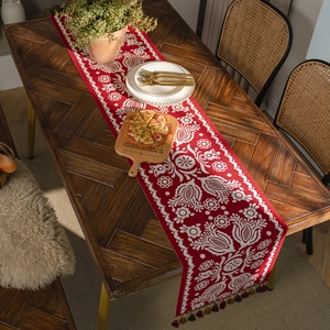 Red jacquard table runner with white ethnic floral patterns and colorful fringe tassels