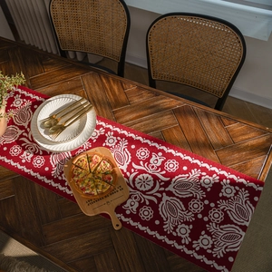 Red jacquard table runner with white floral patterns on a vintage wooden dining table