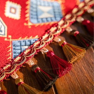 Bohemian style red jacquard table runner with decorative tassel fringe on wood surface