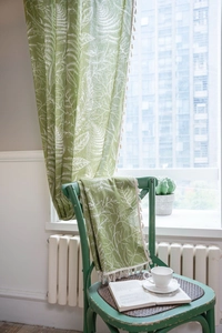 Detailed view of green leaf print curtain fabric with white decorative tassels