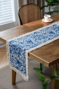 Dettaglio runner da tavola blu e bianco con motivo floreale a farfalla, lino e nappe bianche