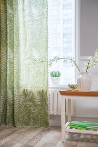 Detail of green leaf pattern curtain fabric with decorative cream pom-pom fringe trim