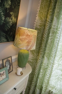 Close-up of green leaf pattern curtain with a botanical ceramic table lamp in warm light