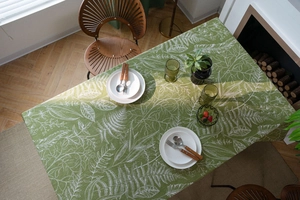 Detailed close-up of a green tablecloth featuring white botanical leaf patterns and cutlery