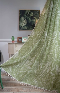 Detail view of green fabric curtain with white leaf print and decorative fringe tassels