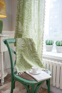 Detail of green curtain fabric with white fern leaf patterns and cream fringe pom-poms