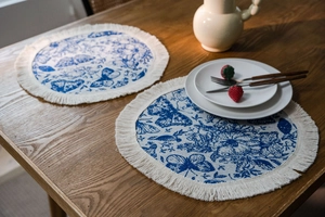 Dettaglio della tovaglietta rotonda con motivi floreali blu e nappe in cotone bianco