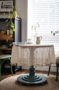 Close-up of beige crochet round tablecloth featuring intricate floral lace and fringe tassels