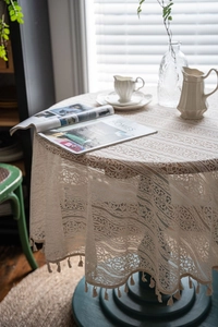 Detail of cream crochet lace tablecloth showing hollow floral patterns and fringe edges