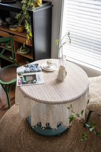 Detailed close-up of beige crochet round tablecloth with lace hollow patterns and tassels