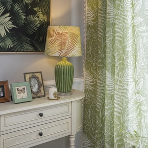 Vintage green ceramic table lamp with tropical palm leaf pattern fabric shade in a cozy room