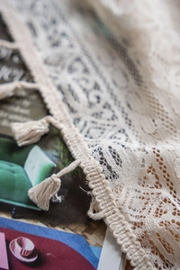 Detailed macro view of beige lace crochet fabric with hollow patterns and fringe tassels