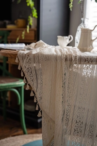 Detailed close-up of vintage crochet lace tablecloth with elegant fringe tassels on wood