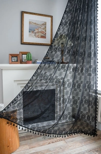 Dettaglio di tende in pizzo nero con motivi floreali traforati e nappe con frange