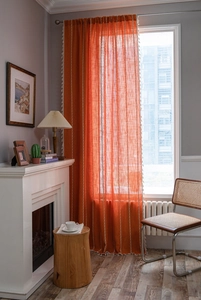 Detail of orange linen curtains with white geometric embroidery and tassel fringe edges