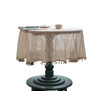 Beige round crochet lace tablecloth with fringe trim on a wooden dining table
