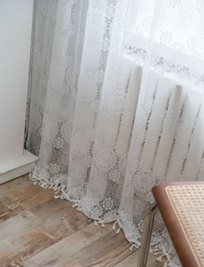Close-up of white crochet lace curtain with hollow floral patterns and delicate fringe trim