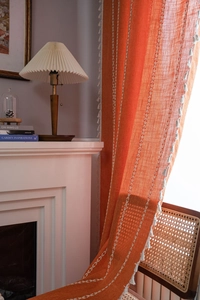 Close-up of orange linen curtain with white diamond embroidery and fringe tassels