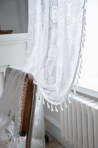 Detail of white crochet lace curtain with floral embroidery and elegant tassel fringe