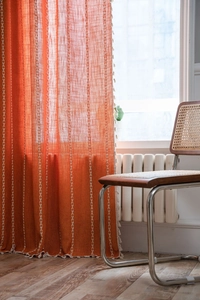 Close-up of terracotta striped curtains with white embroidery and boho tassel fringe