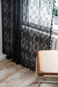 Dettaglio della tenda in pizzo nero con ritagli floreali e bordo a nappa nella luce