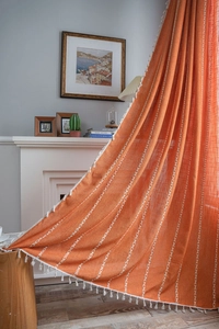 Detail of orange striped cotton linen curtain with white tassel trim and vertical embroidery