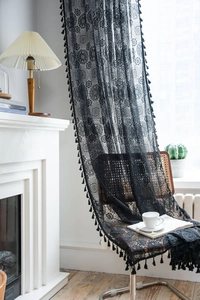 Dettaglio di tenda in pizzo nero con motivi floreali traforati e bordi con nappe