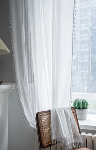 Detail of white semi-transparent crochet curtain with elegant fringe trim and vertical texture