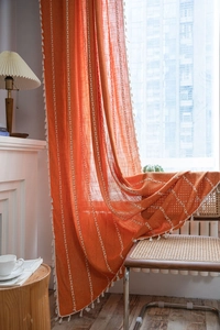 Detail of orange textured curtain with white embroidery patterns and elegant tassels