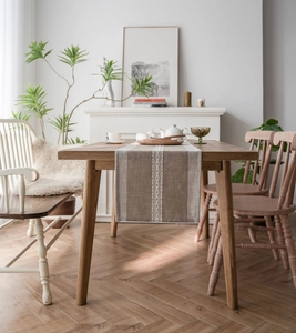 Close-up of bohemian style table runner with white woven pattern on beige fabric texture