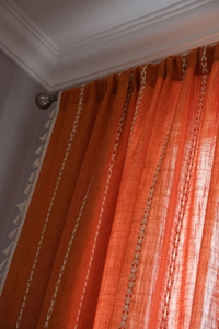 Detail of warm orange linen curtain featuring white V-shaped embroidery and tassel fringe
