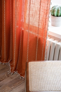 Close-up of orange linen curtain with white embroidery and handmade tassel details