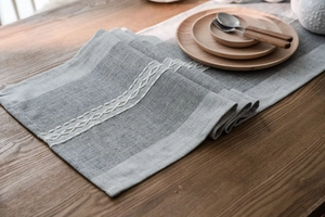 Close-up of grey jacquard table runner with white chain embroidery on a wooden table