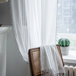 White semi-transparent crochet curtain with tassel trim in a rustic home setting