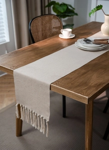 Close-up detail of beige jacquard table runner showing weave texture and tassel fringes
