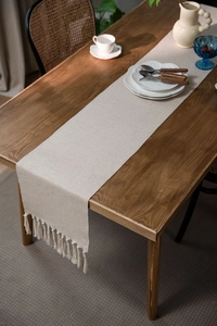 Macro detail of Nordic woven table runner showing thick cream cotton texture and tassels