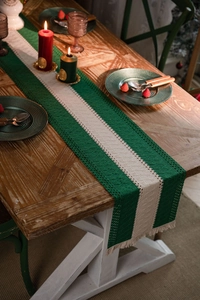 Detail of hand-woven striped table runner with vintage green fringes on a wooden table