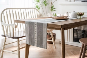 Detail of grey and white linen table runner with intricate white woven chain embroidery