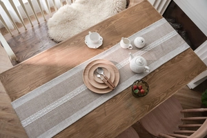 Close-up of Nordic linen table runner with white lace embroidery on a wooden table surface