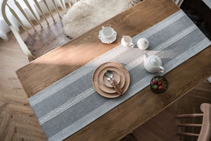 Detail of grey and white striped table runner with intricate white woven lace on dark wood