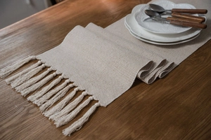 Detail of beige jacquard table runner with honeycomb texture and cotton tassels