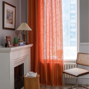 Burnt orange stripe embroidered curtain with white tassels in a cozy rustic room